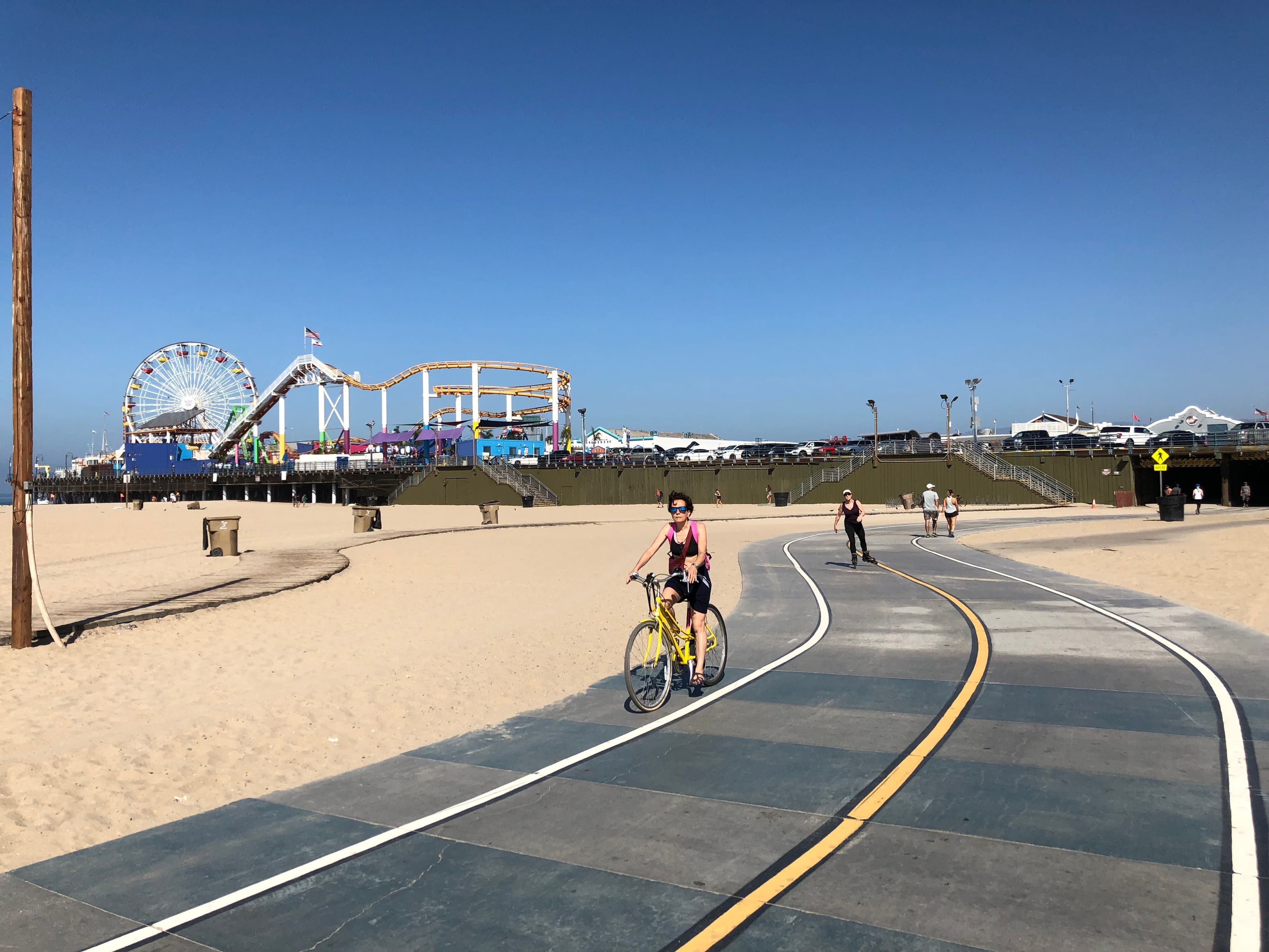 People biking and skating on the Santa Monica beach path with the pier in the background